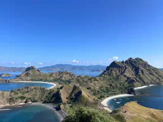 Illustration: A scenic high-angle view of rugged island hills, bays, and beaches under a clear blue sky.