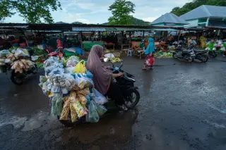 Illustration: A woman on a scooter loaded with packaged market goods drives through an outdoor market.