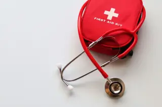 Illustration: A red stethoscope arranged over a red first-aid kit pouch on a plain white surface.