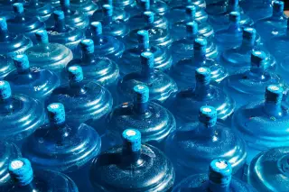 Illustration: Rows of large blue plastic water jugs under bright sunlight.
