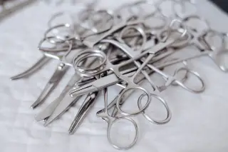 Illustration: A pile of stainless steel surgical scissors and forceps on a white cloth surface.