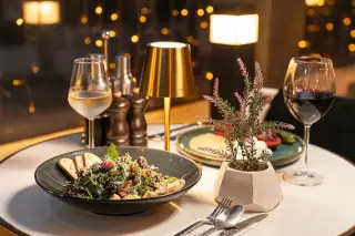 Illustration: A restaurant dining table set with salad, wine glasses, cutlery, and an ambient lamp.