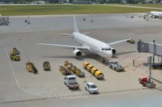 Illustration: A white commercial airplane parked on an airport apron surrounded by ground support vehicles.