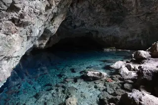 Illustration: Clear turquoise water inside a rocky limestone cave with visible submerged stones.