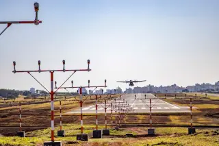 Illustration: An airplane approaches an airport runway lined with approach lighting towers with buildings in the background.