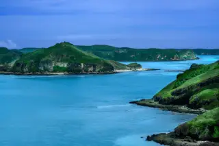 Illustration: A scenic view of green coastal hills surrounded by bright blue ocean water under a cloudy sky.