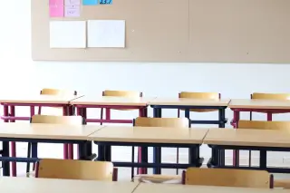 Illustration: Empty wooden desks and chairs inside a brightly lit classroom.