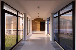 Illustration: An empty, bright indoor corridor with large glass windows and white pillars.