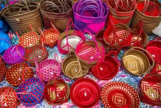 Illustration: Colorful woven baskets and bags arranged closely on a patterned fabric.