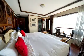 Illustration: A hotel bedroom with a large bed, wooden interior, and balcony overlooking water.