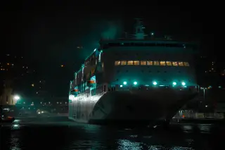 Illustration: A large passenger ferry lit up at night while docked at a port.