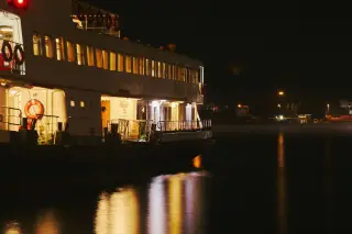 Illustration: The side of a passenger ferry illuminated at night with warm reflections on the water.