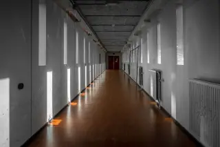 Illustration: An empty indoor corridor lined with narrow vertical windows casting light patterns on the floor.