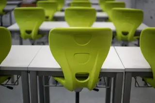 Illustration: Rows of modern lime-green plastic chairs and white desks inside an empty classroom.