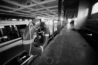 Illustration: Monochrome shot of a ferry interior showing a lifebuoy beside vehicles and passengers.