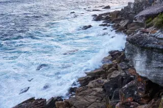 Illustration: Ocean waves crash against rugged rocky cliffs along a coastline.