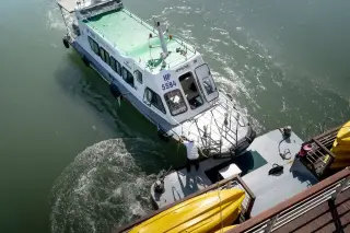 Illustration: A passenger boat docks alongside a platform as a crew member pulls the mooring line.