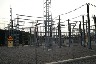 Illustration: An outdoor electrical substation with steel structures and power lines behind a chain-link fence.