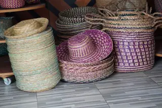 Illustration: Stacks of woven straw hats and patterned baskets arranged on a tiled floor.