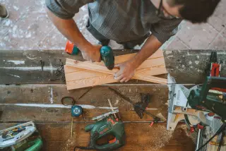Illustration: A high-angle view of a person drilling wooden planks on a workbench with power tools.