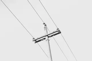 Illustration: A wooden utility pole with crossarms and wires against a plain pale sky.