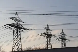 Illustration: High-voltage electricity transmission towers and power lines silhouetted against a pale sky.
