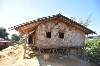 Illustration: A simple rural stilt house with woven bamboo walls on a dry hillside.