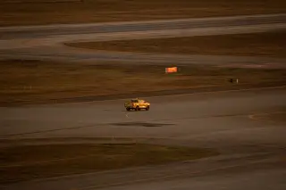 Illustration: A yellow pickup truck drives across an airport runway and taxiway in warm light.