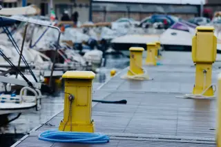Illustration: Yellow utility pedestals and bollards line a marina dock beside moored motorboats.