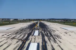 Illustration: A view looking down an airport runway blocked by a yellow cross closure marker under a clear sky.