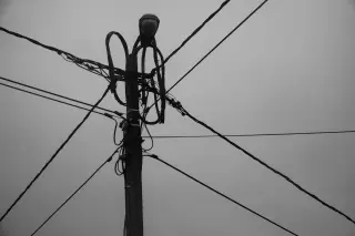 Illustration: A black and white close-up of a utility pole with tangled wires against a dull sky.