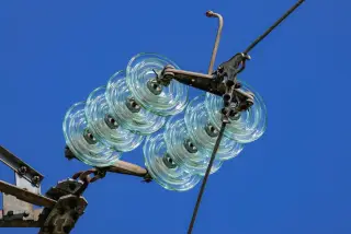 Illustration: Close-up of clear glass disc insulators mounted on power lines against a clear blue sky.