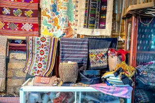Illustration: A display of colorful woven textiles and baskets hung and arranged in a shop.
